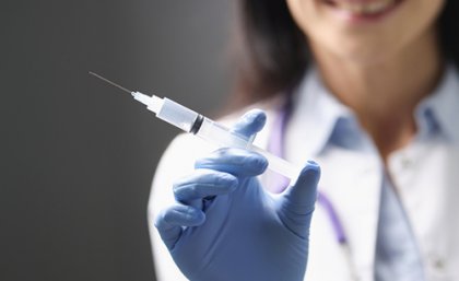 Close up of gloved woman's hand holding a syringe, with her trunk blurred in the background.